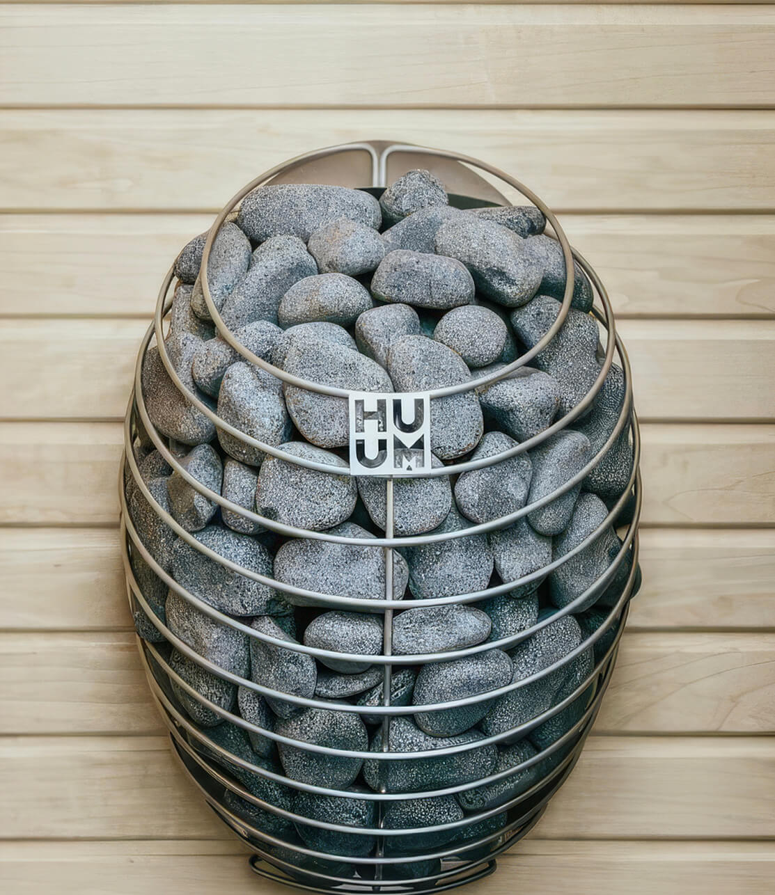 HUUM DROP sauna heater filled with rounded grey sauna stones against pale cedar cladding